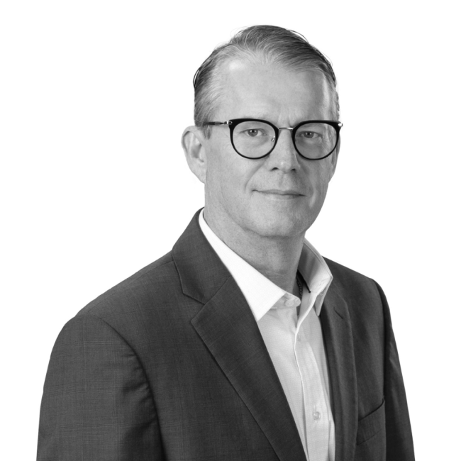 Black-and-white portrait of a middle-aged man with glasses, wearing a suit and white shirt, looking at the camera with a slight smile.