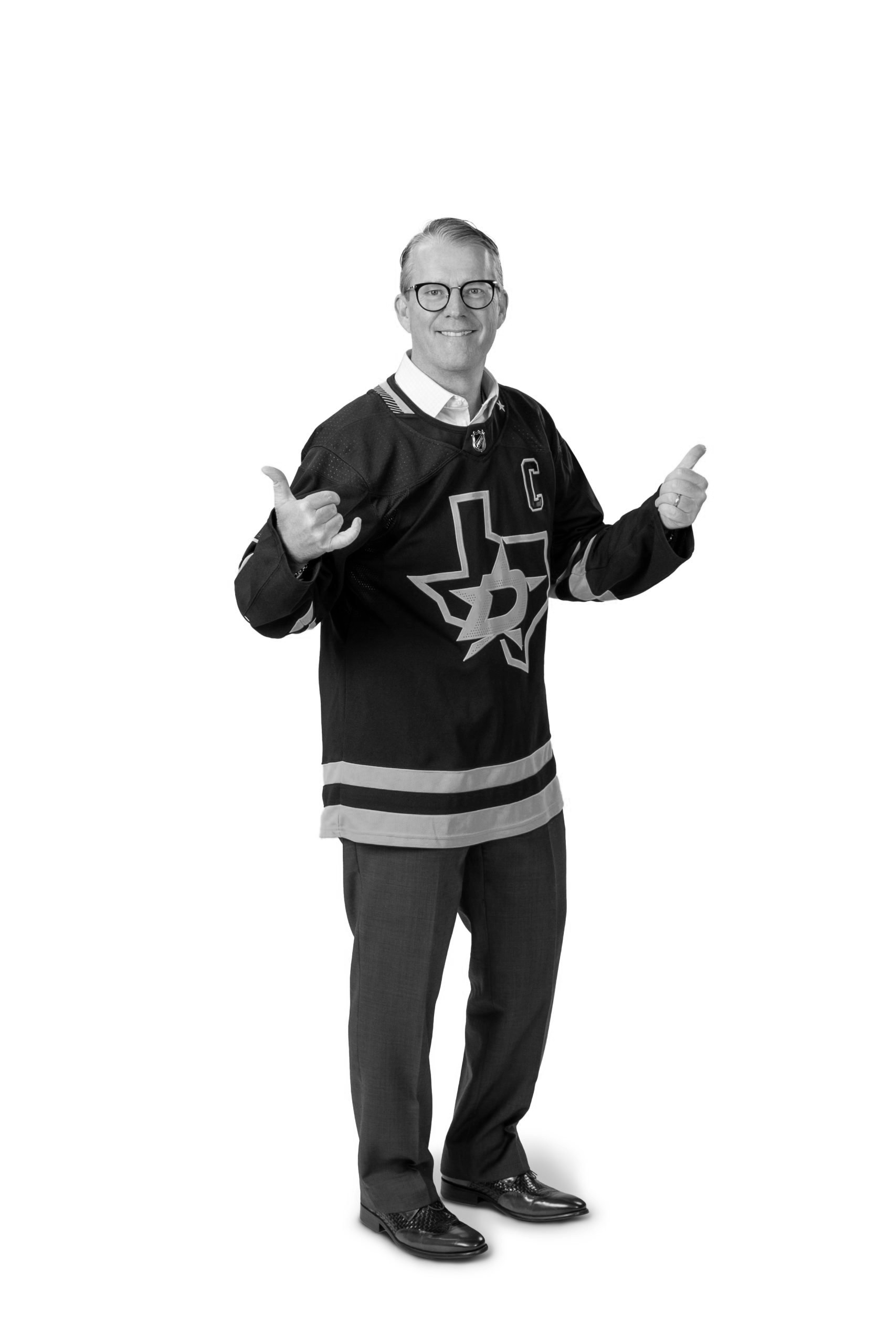 A man in a hockey jersey celebrating, smiling, wearing glasses, giving a thumbs-up with both hands, against a plain white background.