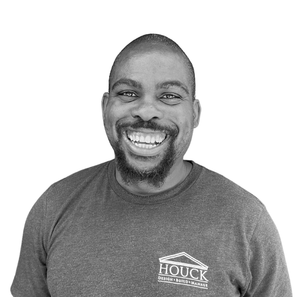 Portrait of a smiling man with a beard and short hair, wearing a dark T-shirt with the logo 'HOUCK DESIGN·BUILD·MANAGE' on it, against a plain white background.