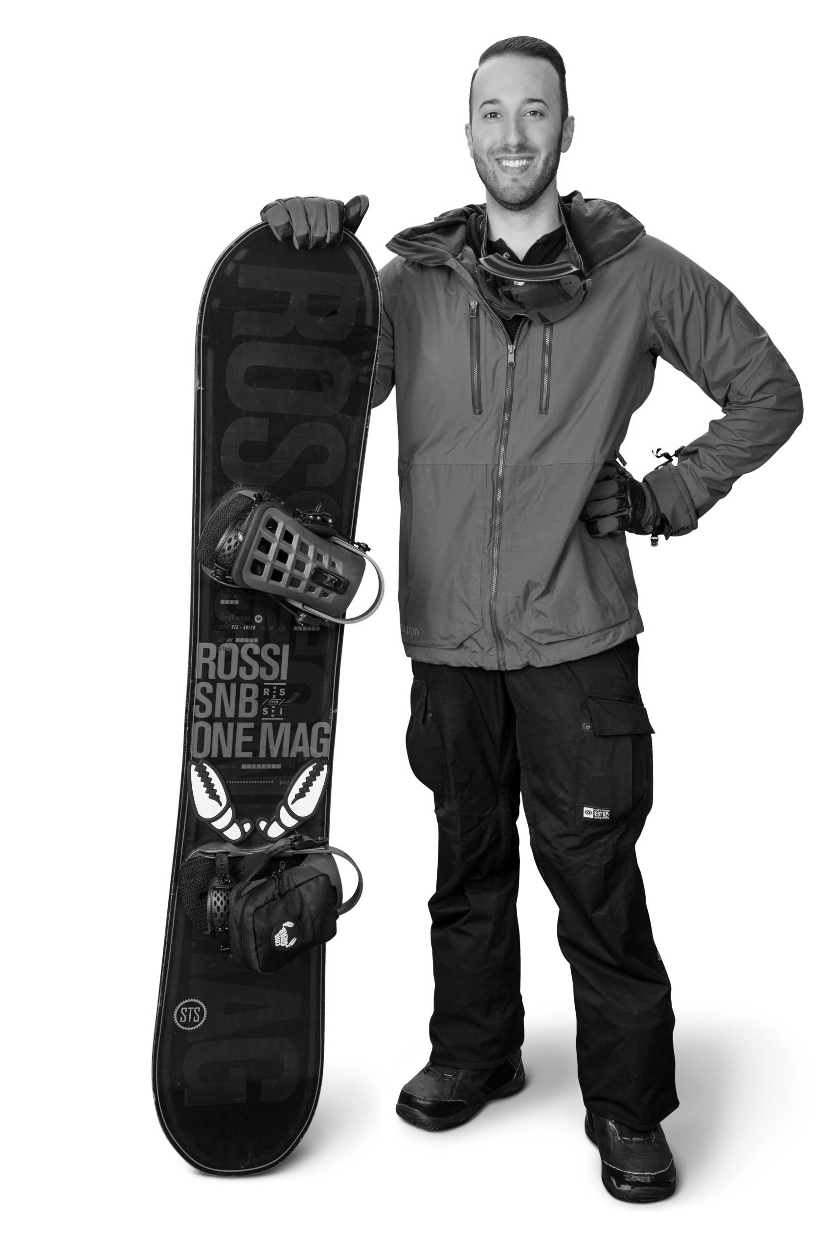 A man dressed in winter snowboarding gear holding a snowboard and smiling at the camera.