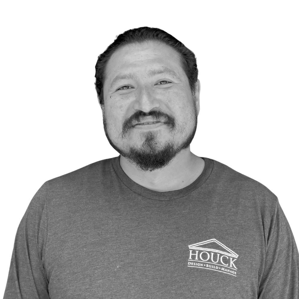 Black and white photo of a man with a beard, smiling, wearing a T-shirt with 'Houck Design Build Manage' logo.