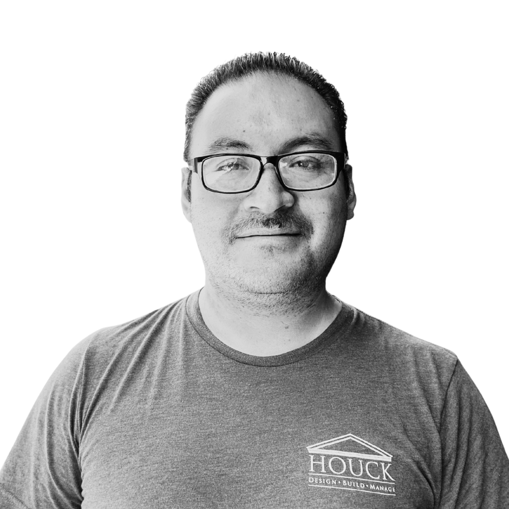 A man with glasses and a beard is wearing a t-shirt with the text 'HOUCK Design Build Manage' on it, and smiling in front of a plain white background.