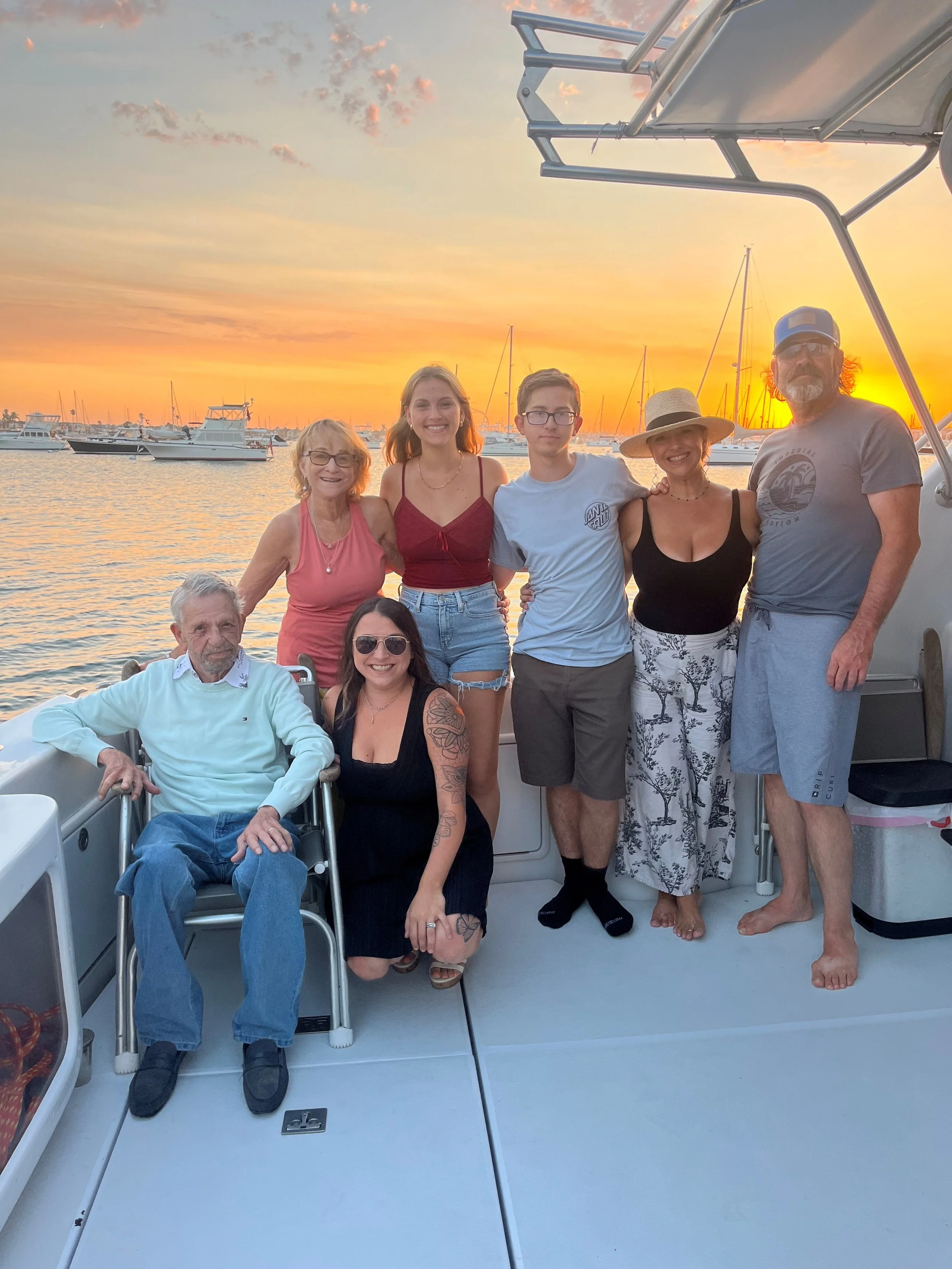 Group of seven people on a boat during sunset, with sailboats in the background.