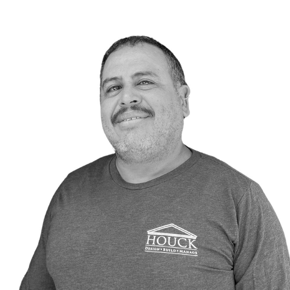 A man posing for a photo, smiling slightly, wearing a dark t-shirt with the logo 'HOUCK DESIGN BUILD MANAGE' on it, against a plain white background.