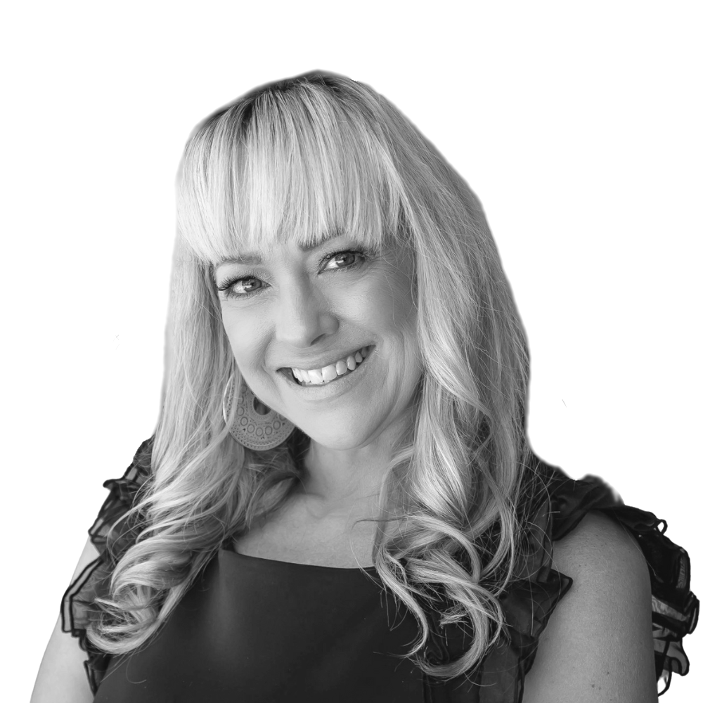 Black-and-white portrait of a smiling woman with long, wavy hair and bangs, wearing a sleeveless top with ruffled shoulders and large circular earrings.