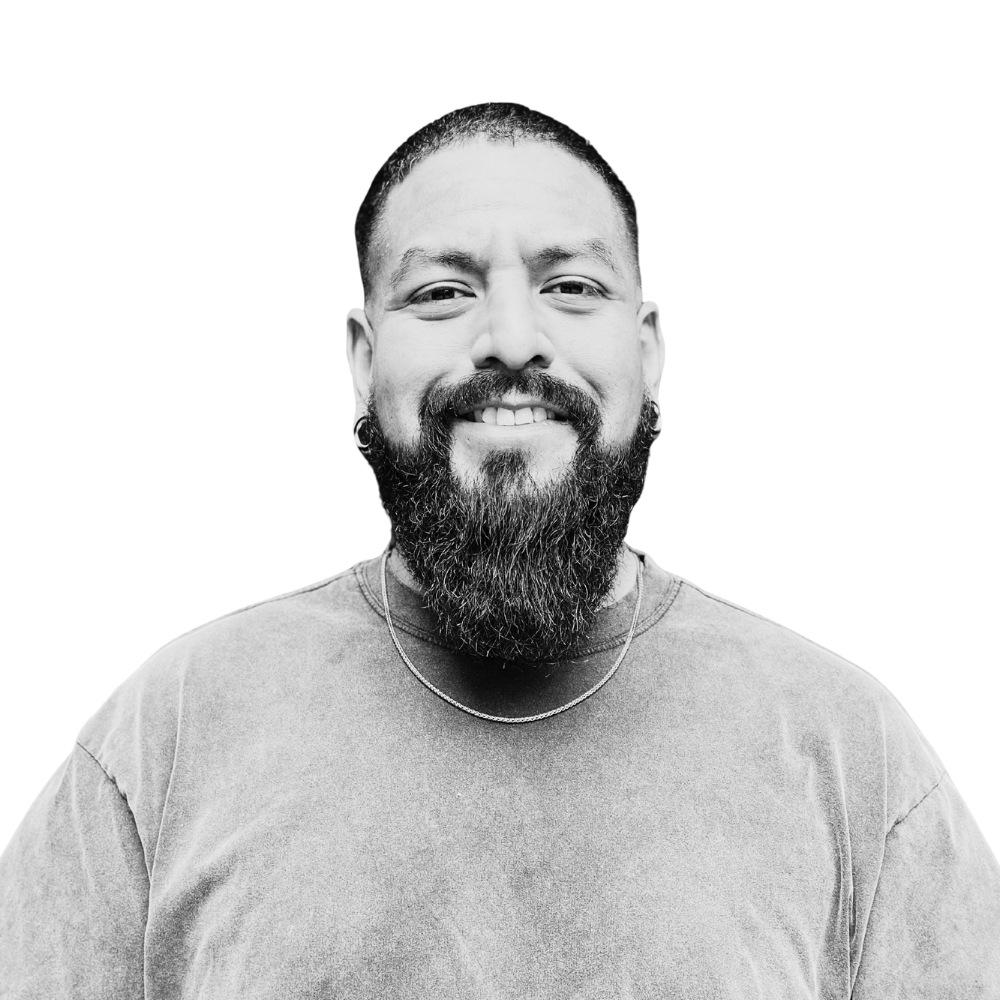 Black and white close-up portrait of a man with a beard, mustache, earrings, a short haircut, and a chain necklace, smiling at the camera.