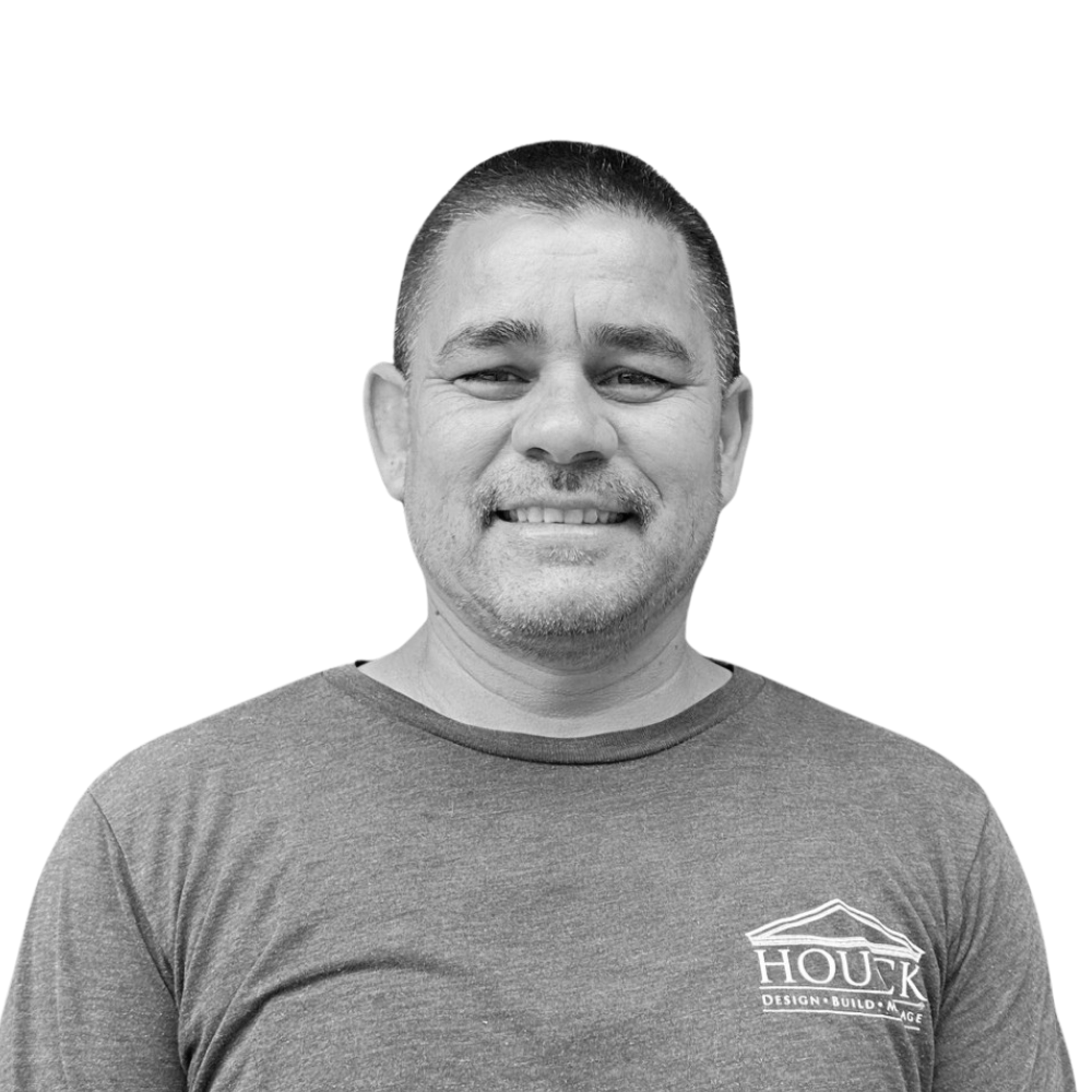 A man smiling in a black-and-white photo, wearing a T-shirt with a house logo and text.