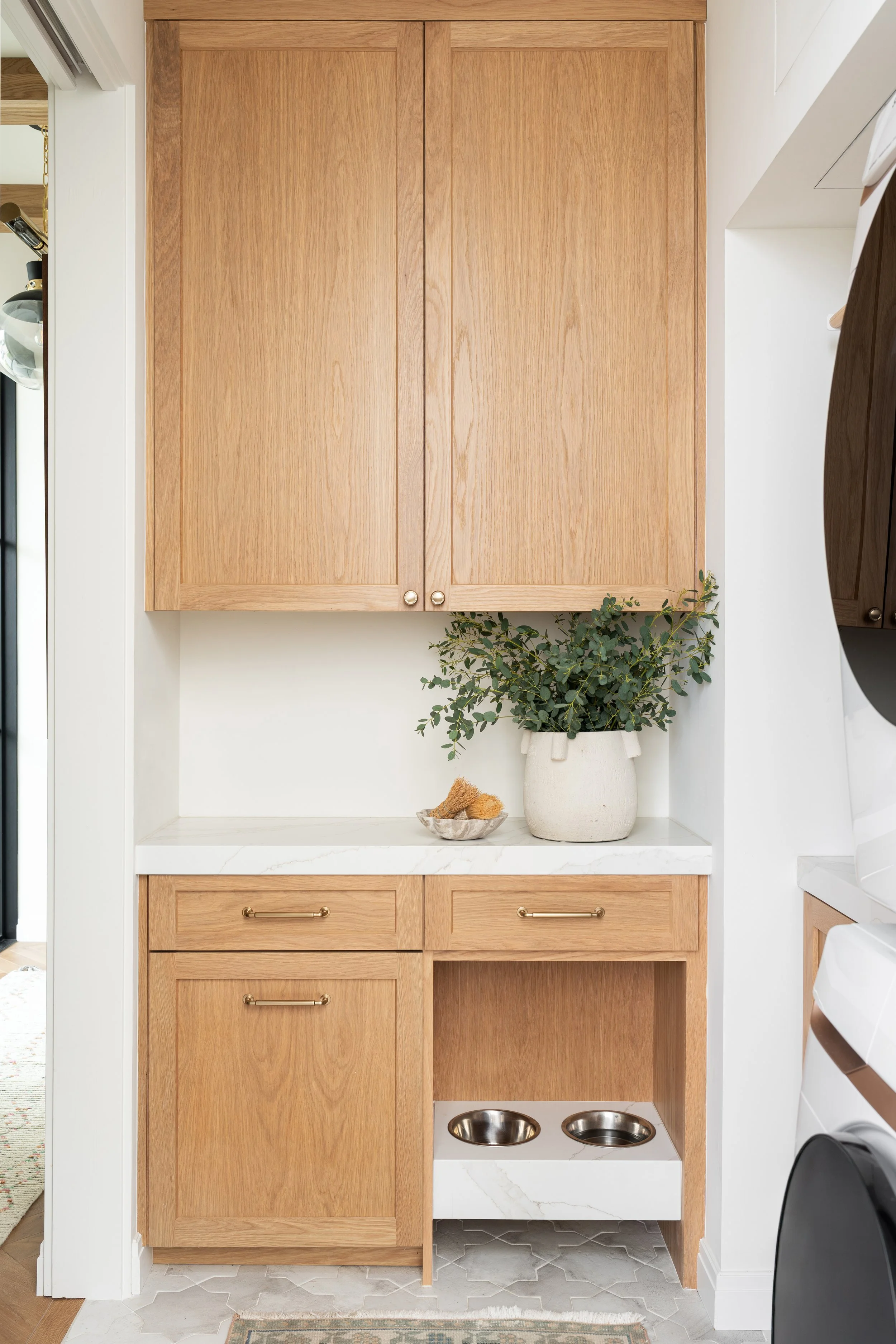 Built-in dog feeding station tucked into oak laundry room cabinetry by Allito Spaces