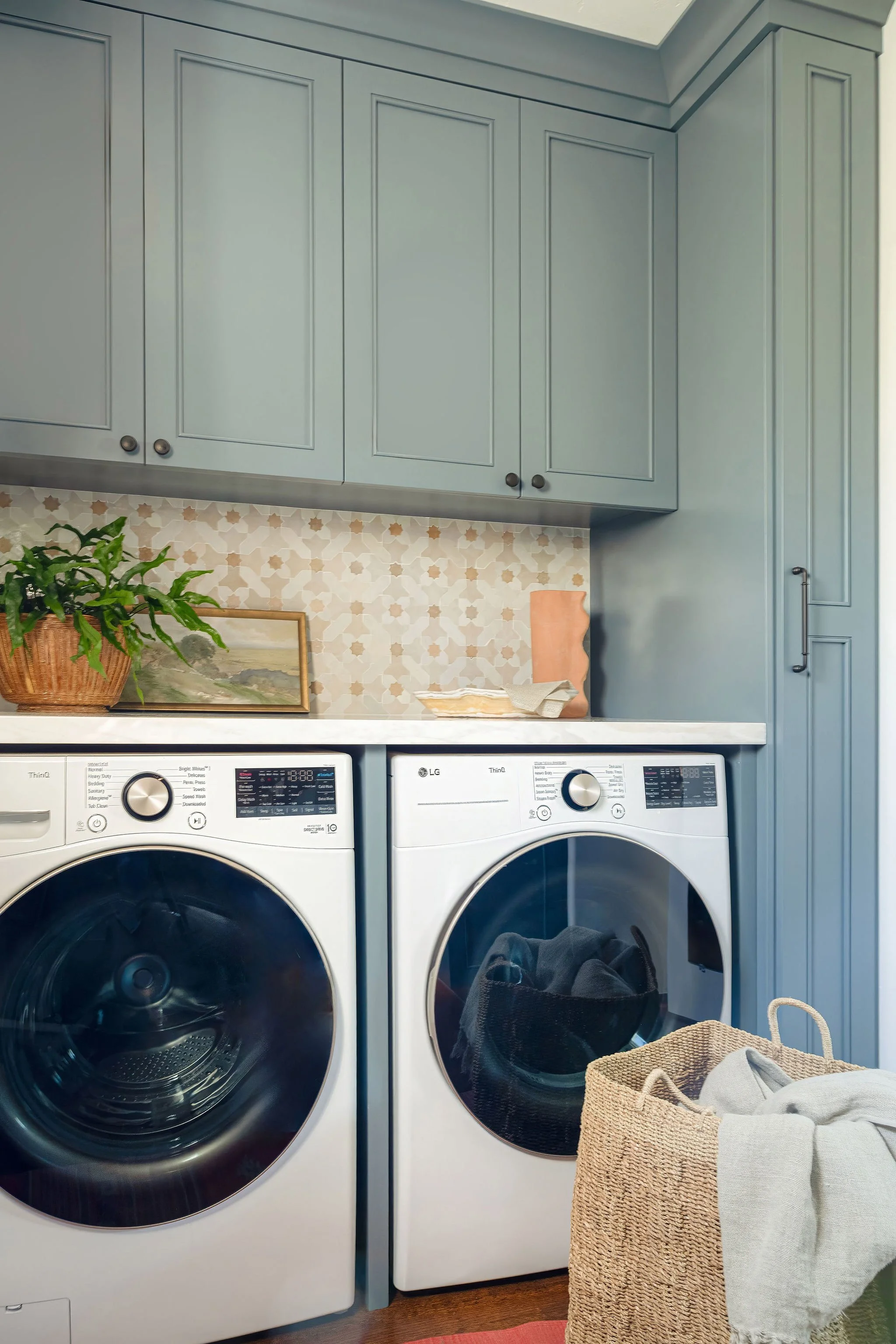 Custom blue laundry room in a spanish style home using a zellige mosaic backslash with terracotta accents.  Small storage for ironing board.
