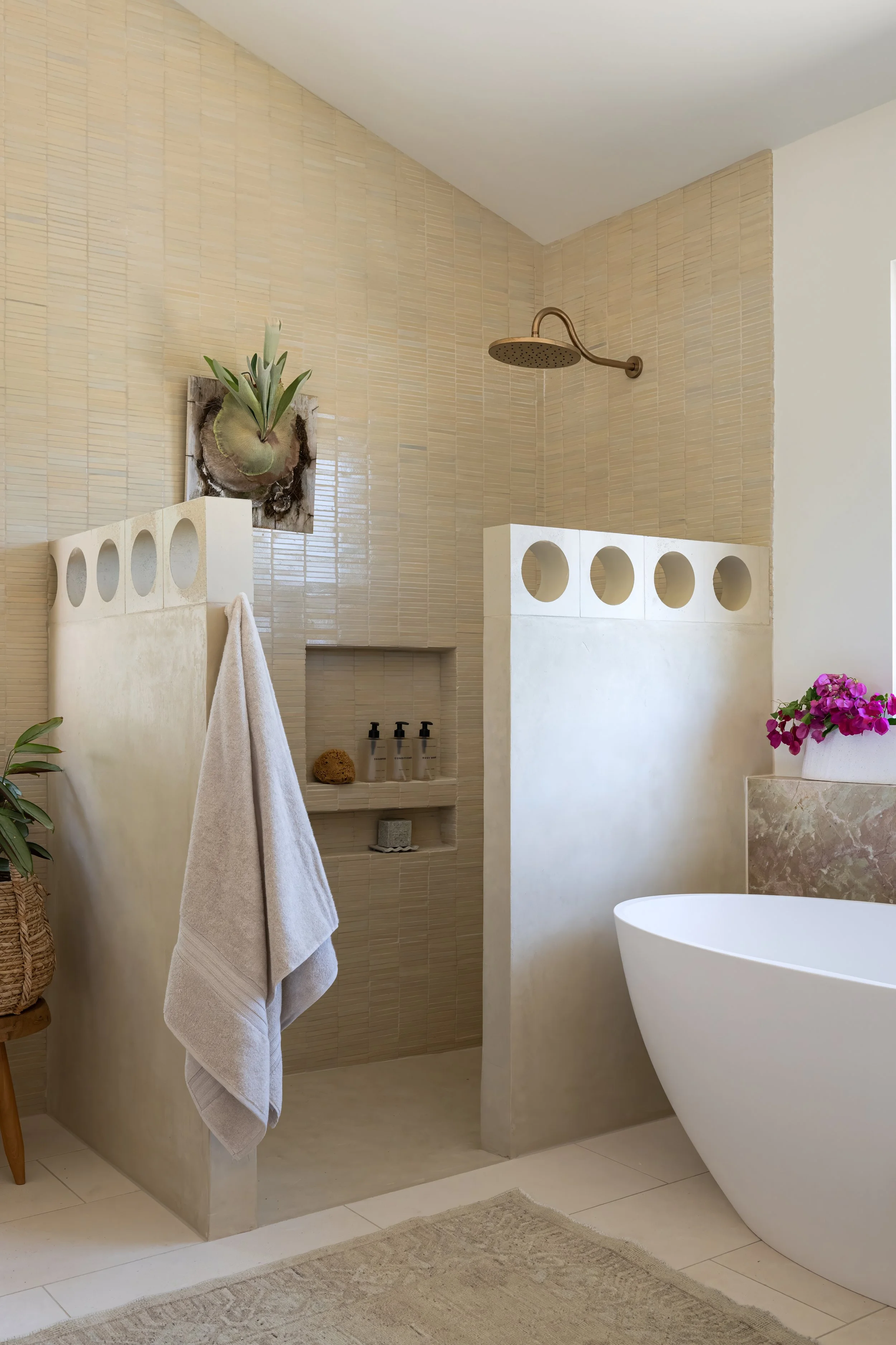 This is a freestanding tub in a modern organic bathroom, with micro cement floors and a marble accents.   There are matchstick tiles on the wall and a vaulted ceiling.  It has a breezy and spa like feeling using a vintage rug and breeze blocks.