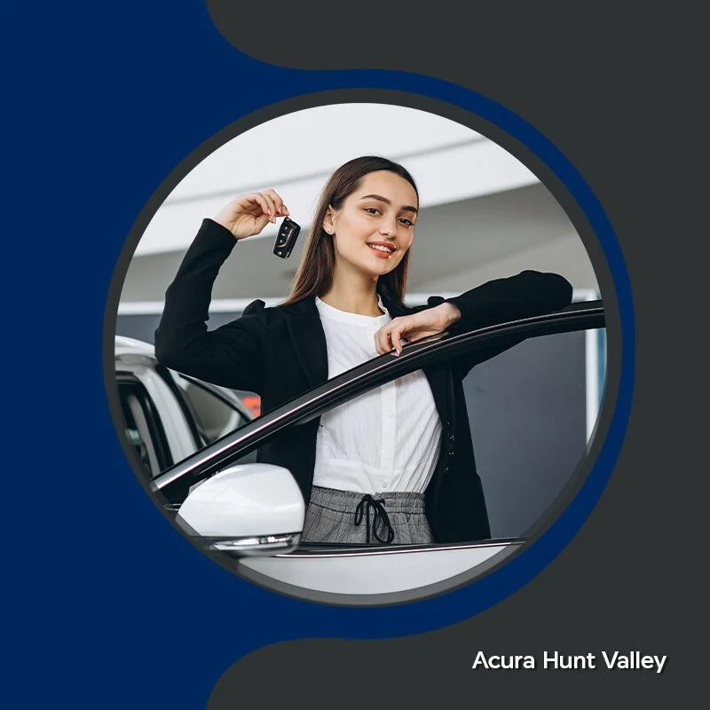A woman in business attire holding a car key while leaning on a white car inside a dealership, smiling at the camera.