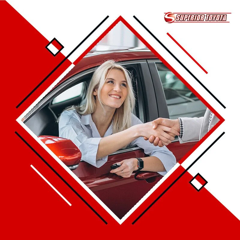 A woman with blonde hair smiling while shaking hands with another person in a car dealership. The woman is sitting in a red car, and the background shows a sales environment.