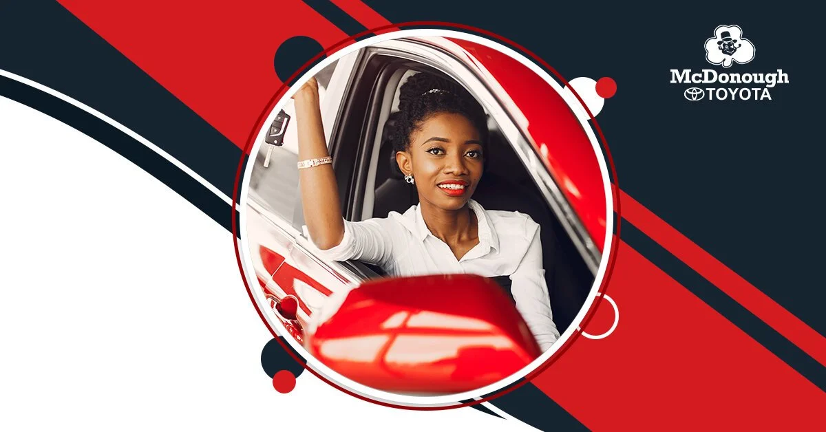 A woman sitting in a red car with a McDonough Toyota logo in the background, smiling and looking at the camera.