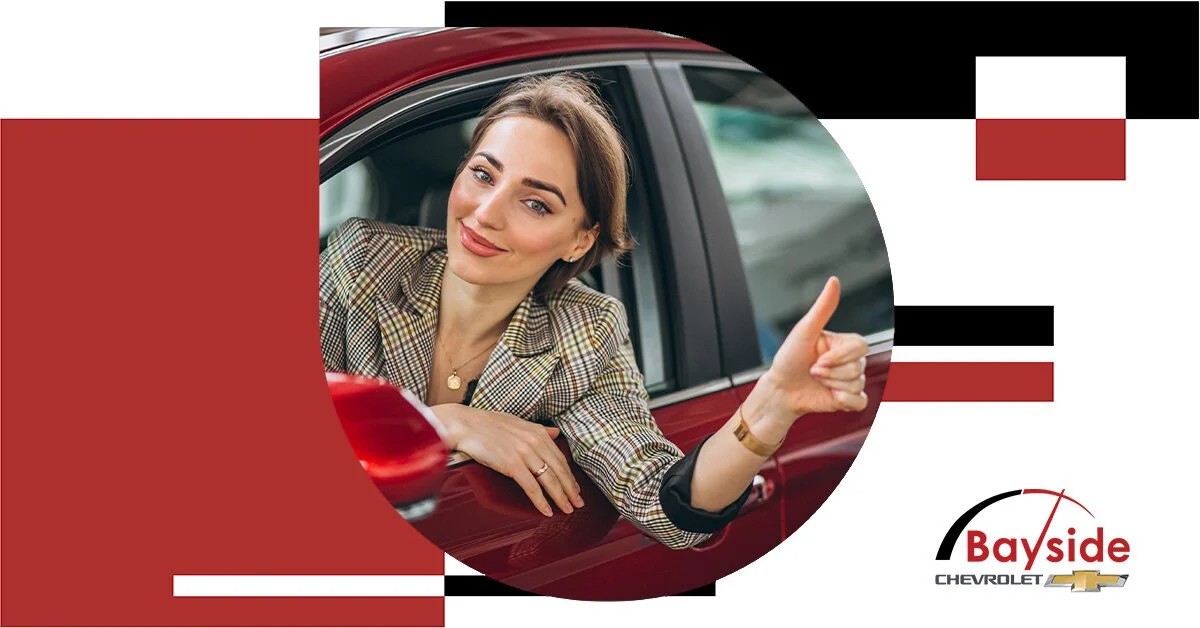 Woman in business attire sitting in a red Chevrolet car window, giving a thumbs-up, with Bayside Chevrolet logo below.