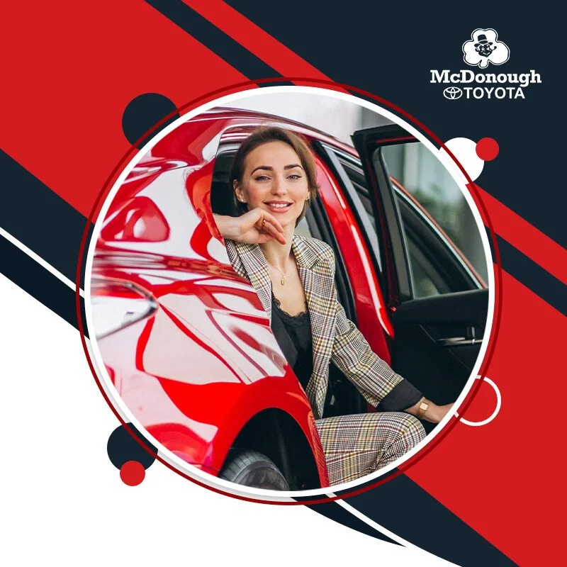 A woman in a plaid suit sitting inside a red car, leaning out of the open door, smiling.