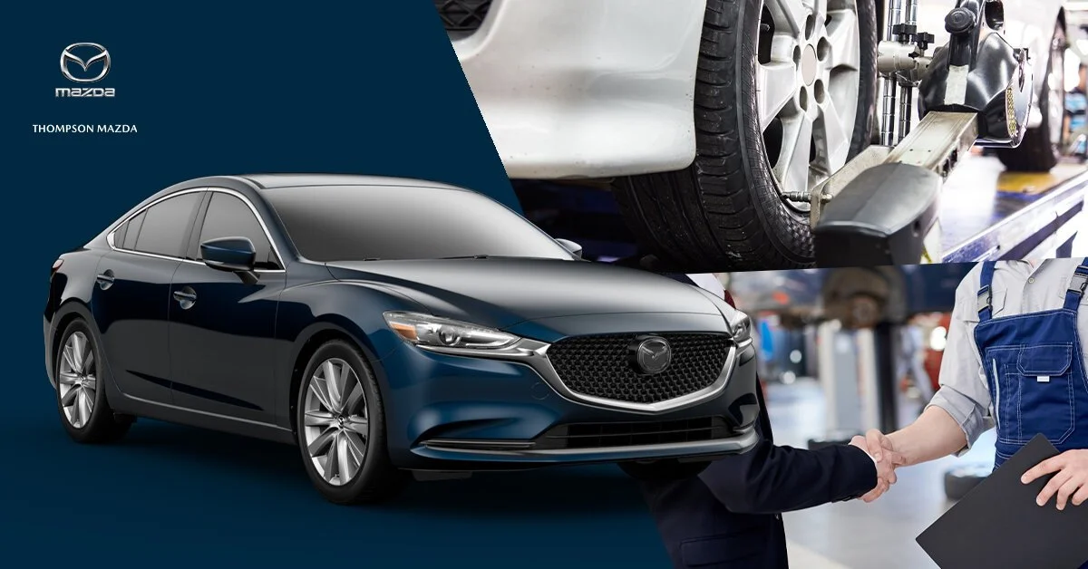 A new black sedan car with a Mazda logo on the front grille, and an automotive workshop in the background showing a wheel being worked on, with a mechanic and a customer shaking hands.