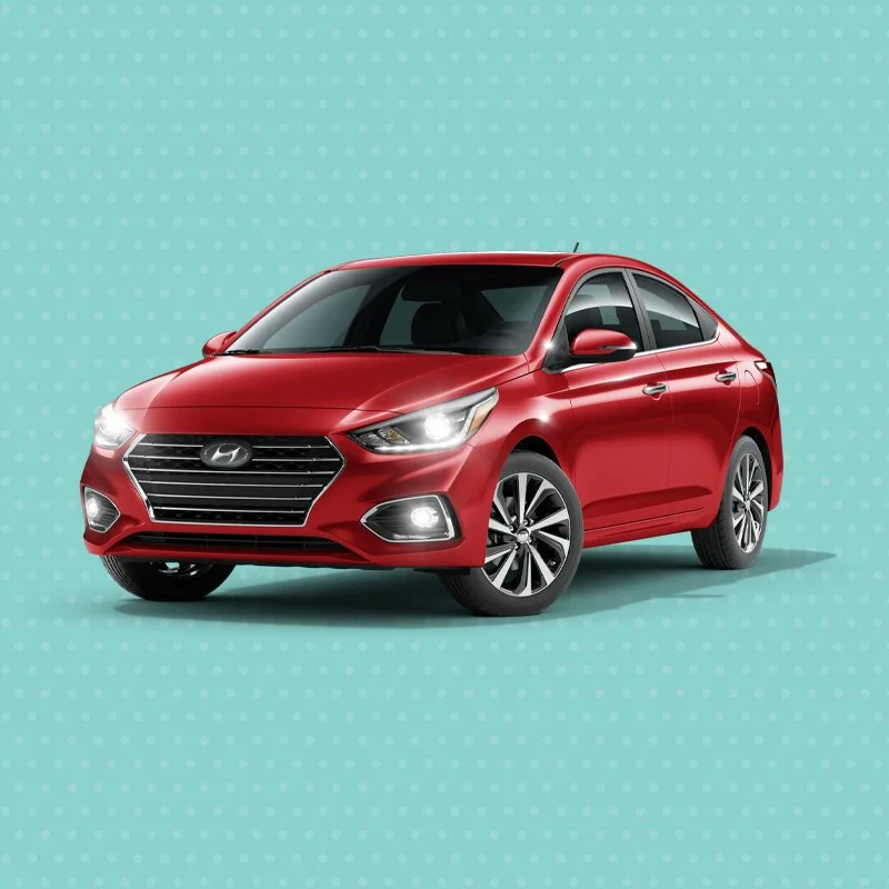 Red Hyundai sedan car with headlights on, positioned against a teal background with polka dots.