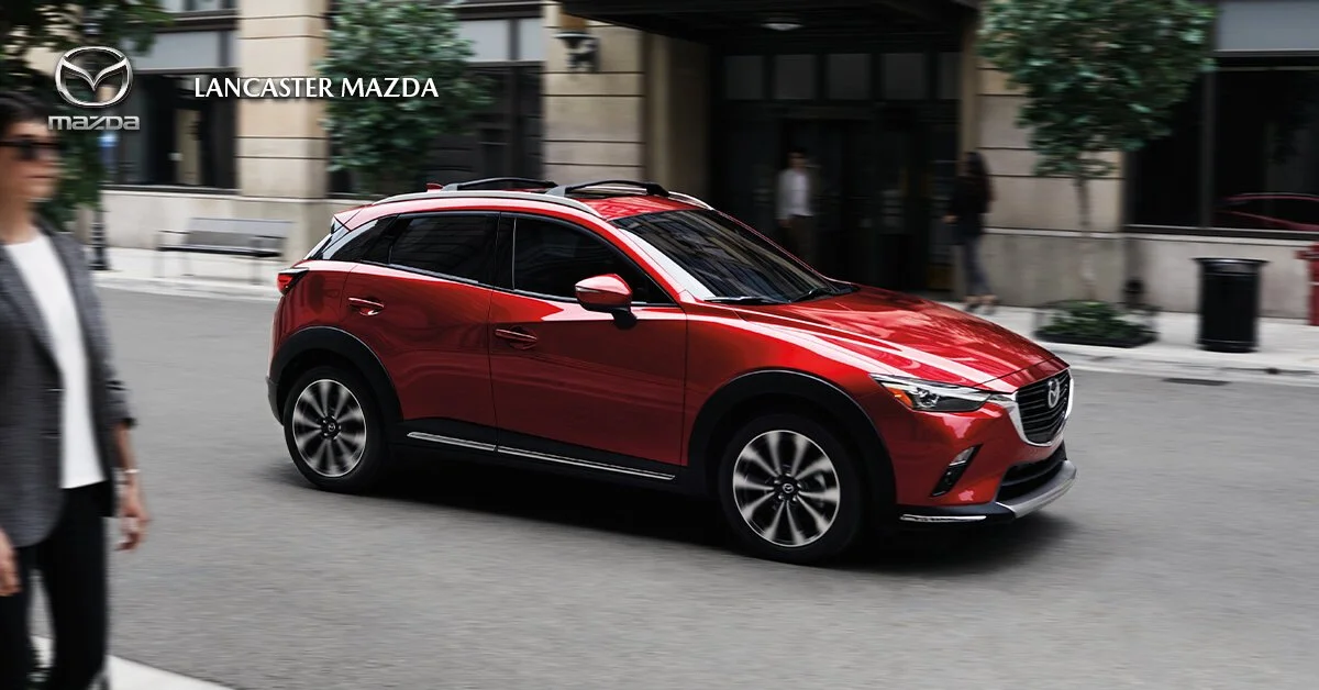 Red Mazda SUV driving on city street near Lancaster Mazda dealership.