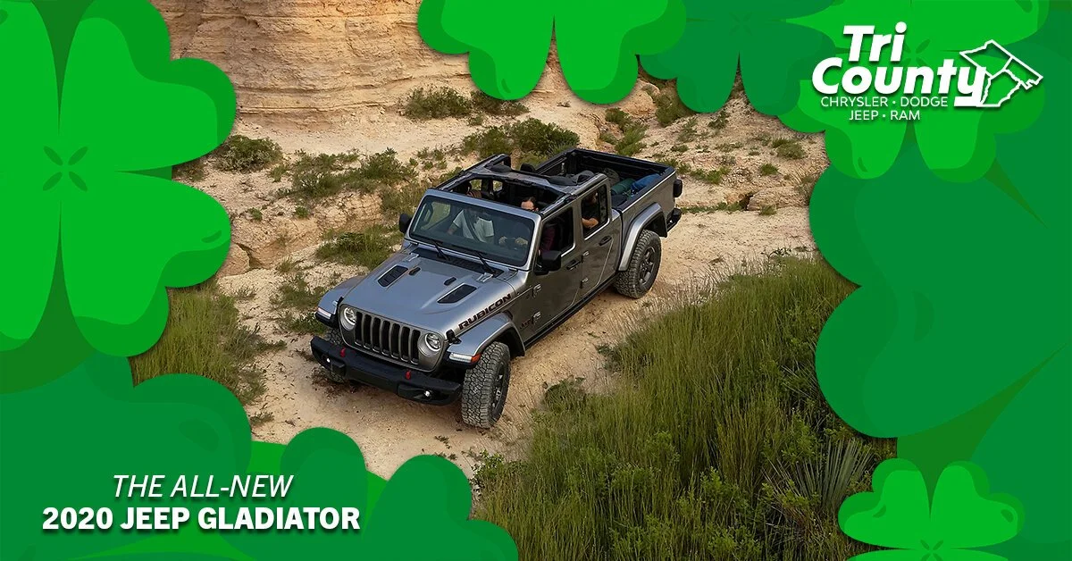 A 2020 Jeep Gladiator Rubicon off-road vehicle driving on a dirt trail with green grass and rocky terrain, framed by green shamrock graphics and dealership branding.