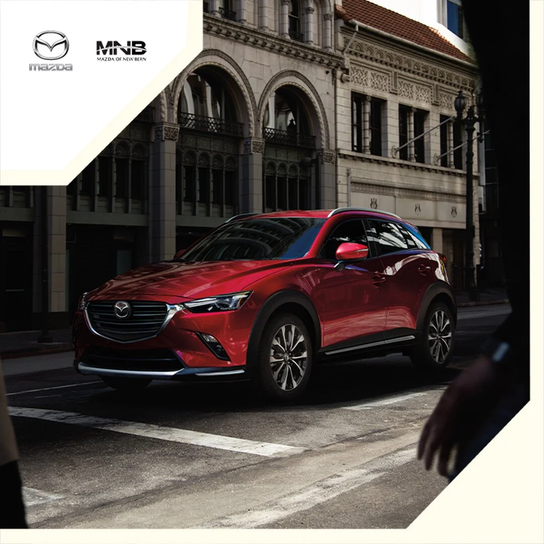 A red Mazda SUV parked on a city street in front of historic buildings.