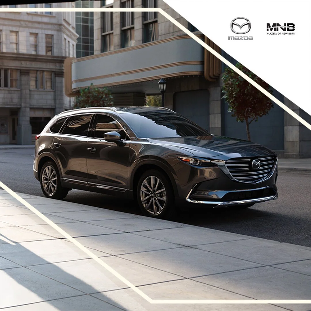 Black Mazda SUV parked on city street with buildings in the background.