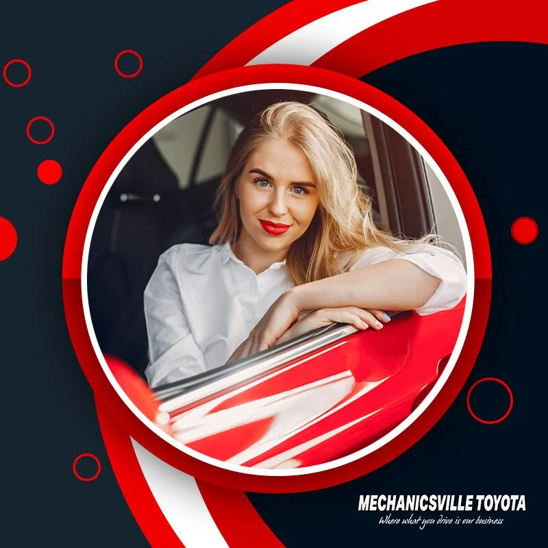 A woman with blonde hair and red lipstick sitting in a red car, smiling at the camera.