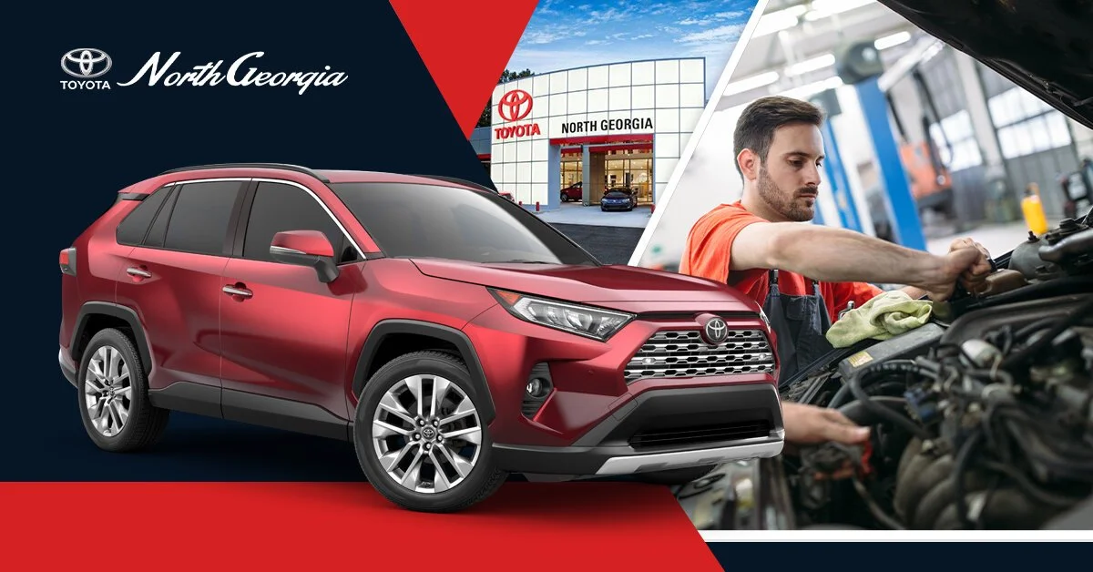 A red Toyota SUV parked in front of a North Georgia Toyota dealership, with a mechanic inspecting a car engine inside the service center.