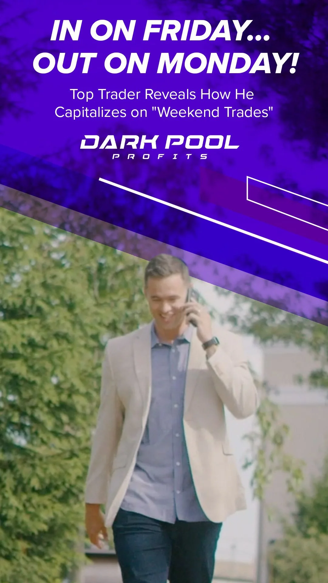 A man in a beige blazer and blue shirt talking on a cellphone while walking outdoors with green trees in the background.