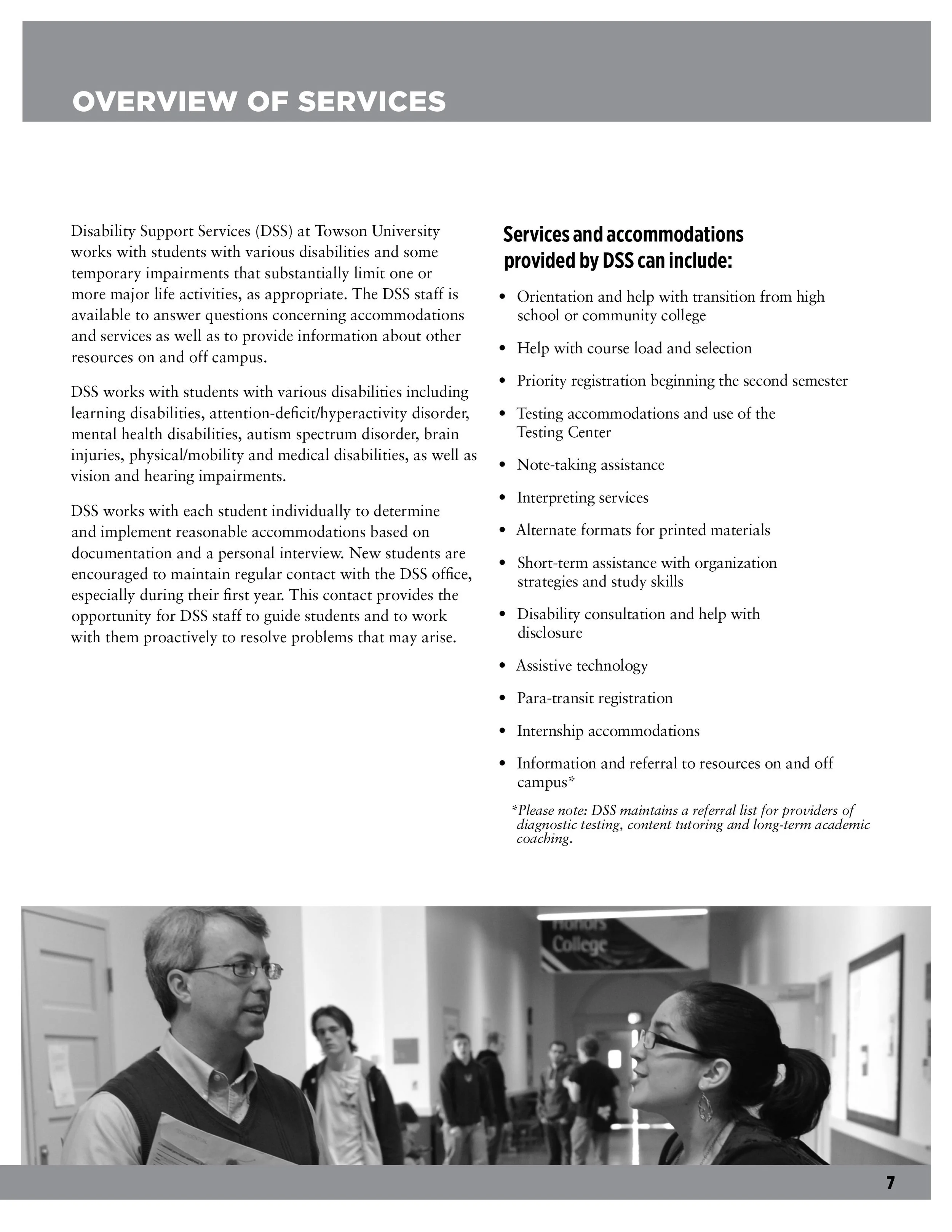 A black and white photograph of a man and woman talking in a hallway at a college, with several students walking in the background.