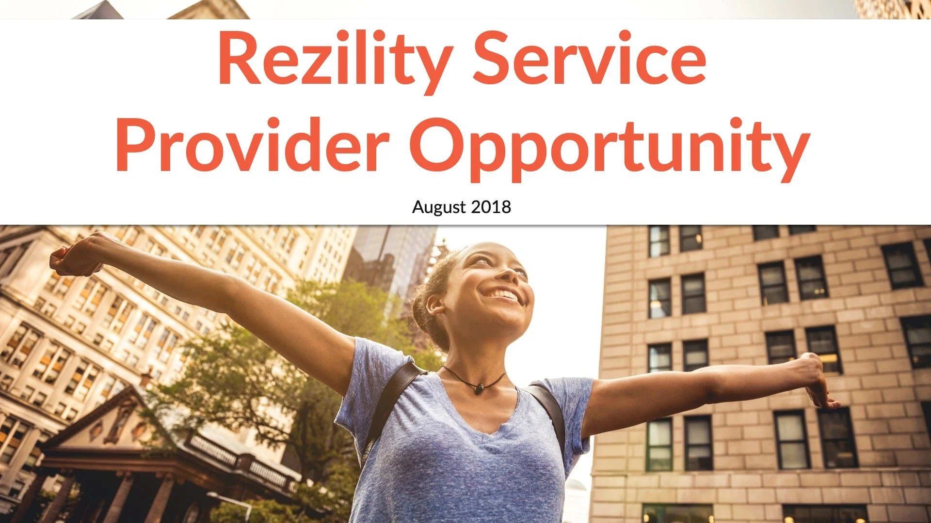 A woman standing outdoors with arms outstretched and smiling, surrounded by city buildings.