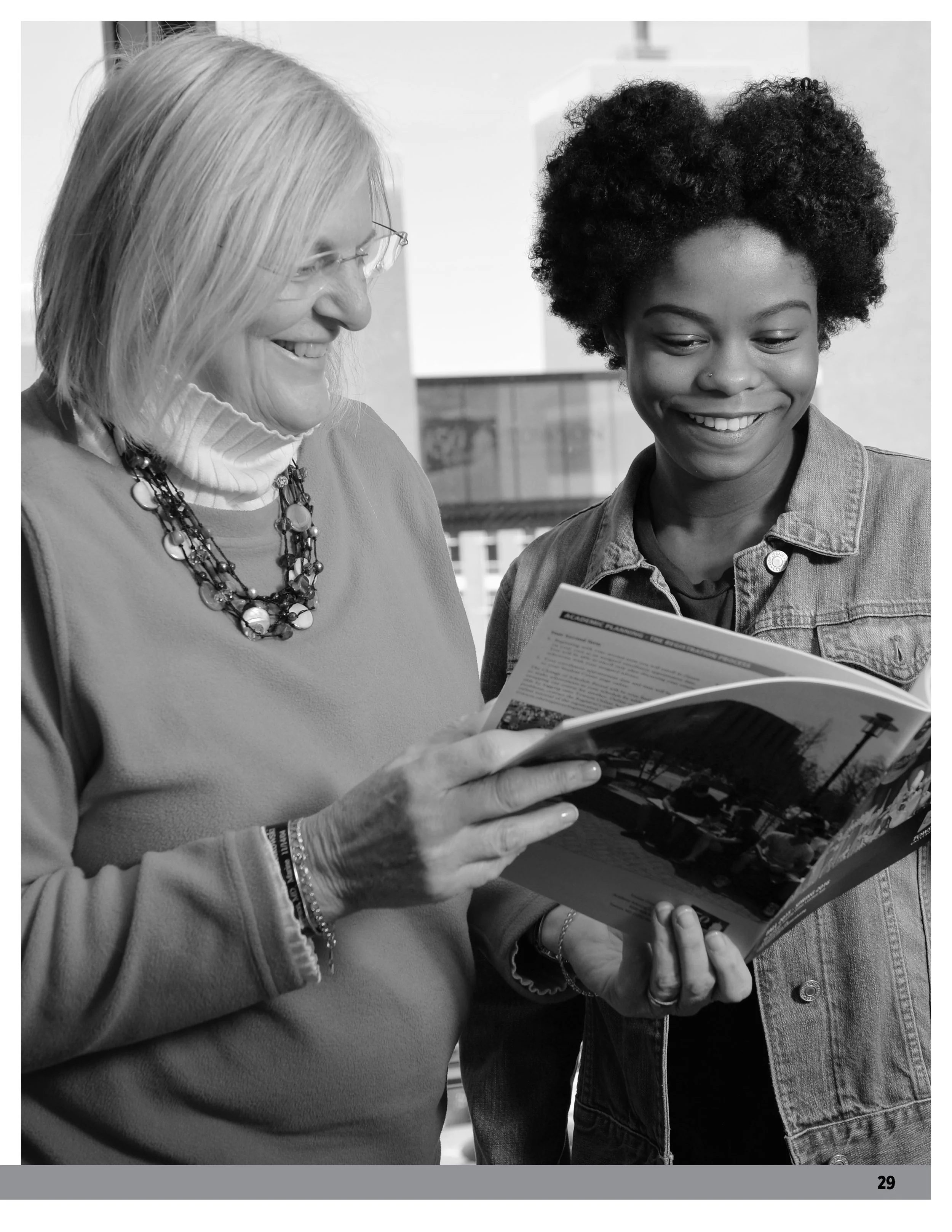 Two women looking at a magazine together, laughing and smiling.