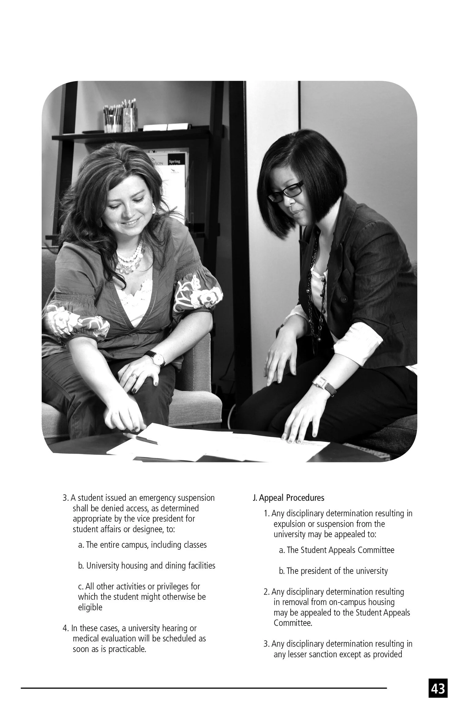 Black and white photo of two women sitting at a table, examining documents, in an office or academic setting.