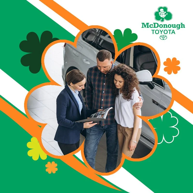 A couple is looking at a car brochure with a car in the background at a Toyota dealership, with a saleswoman smiling and explaining.