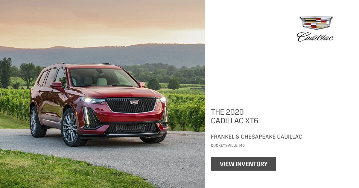 Red 2020 Cadillac XT6 SUV parked on a rural road with green fields and hills in the background during sunset.