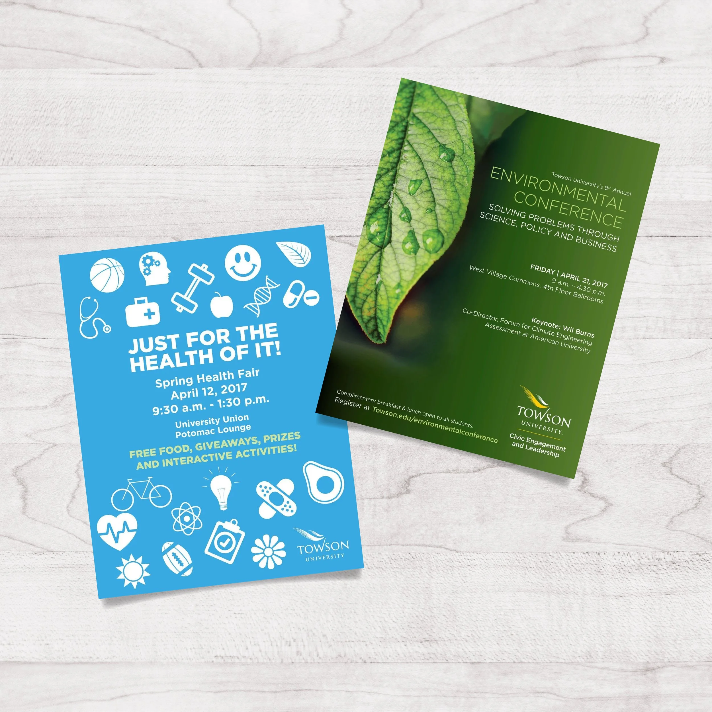 Two flyers on a light wooden surface. The blue flyer promotes a Spring Health Fair at Towson University with free food, giveaways, prizes, and activities, scheduled for April 12, 2017. The green flyer advertises Towson University's 8th Annual Environ
