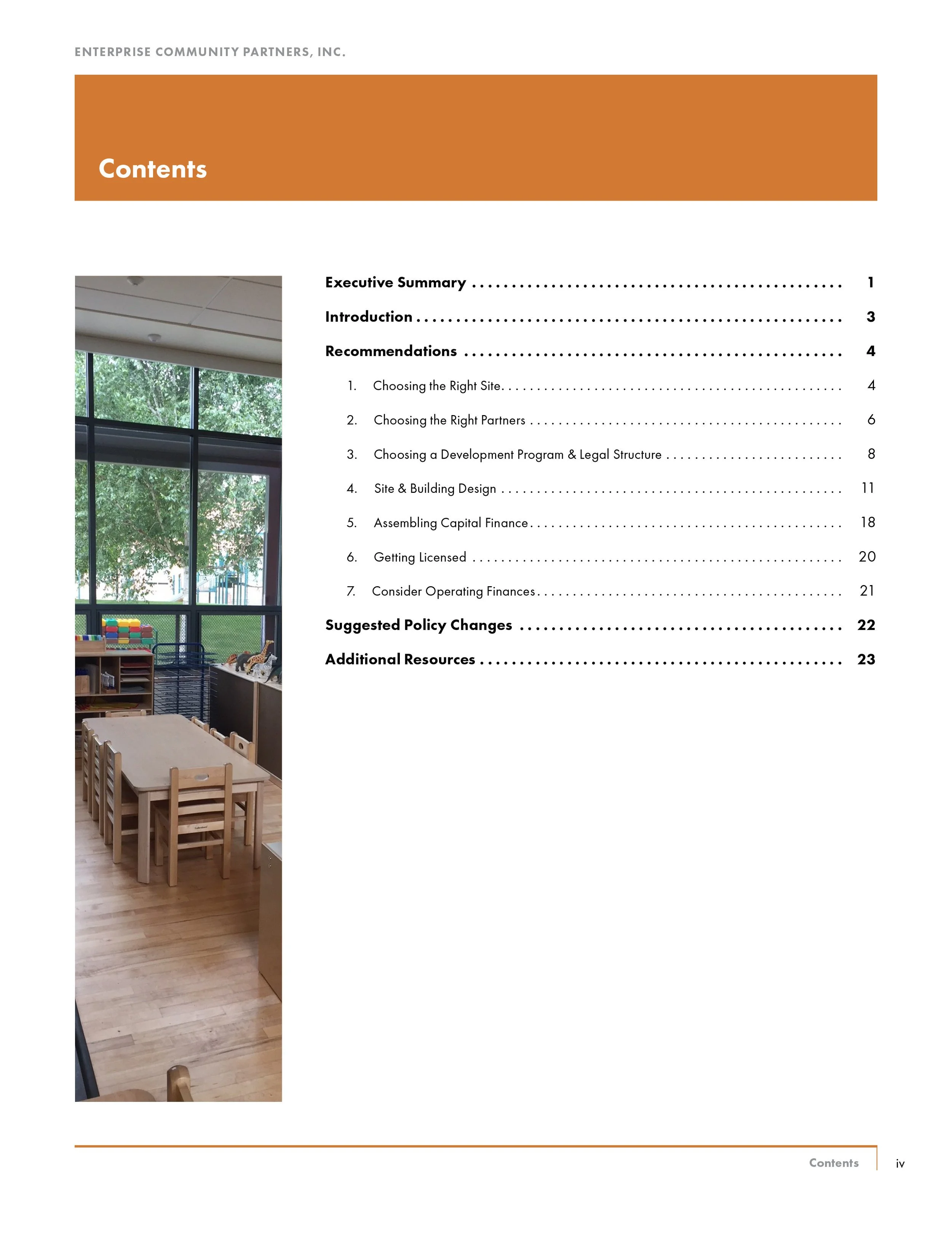 Table and chairs with a large window showing trees outside, inside a room with wood flooring and bookshelves.
