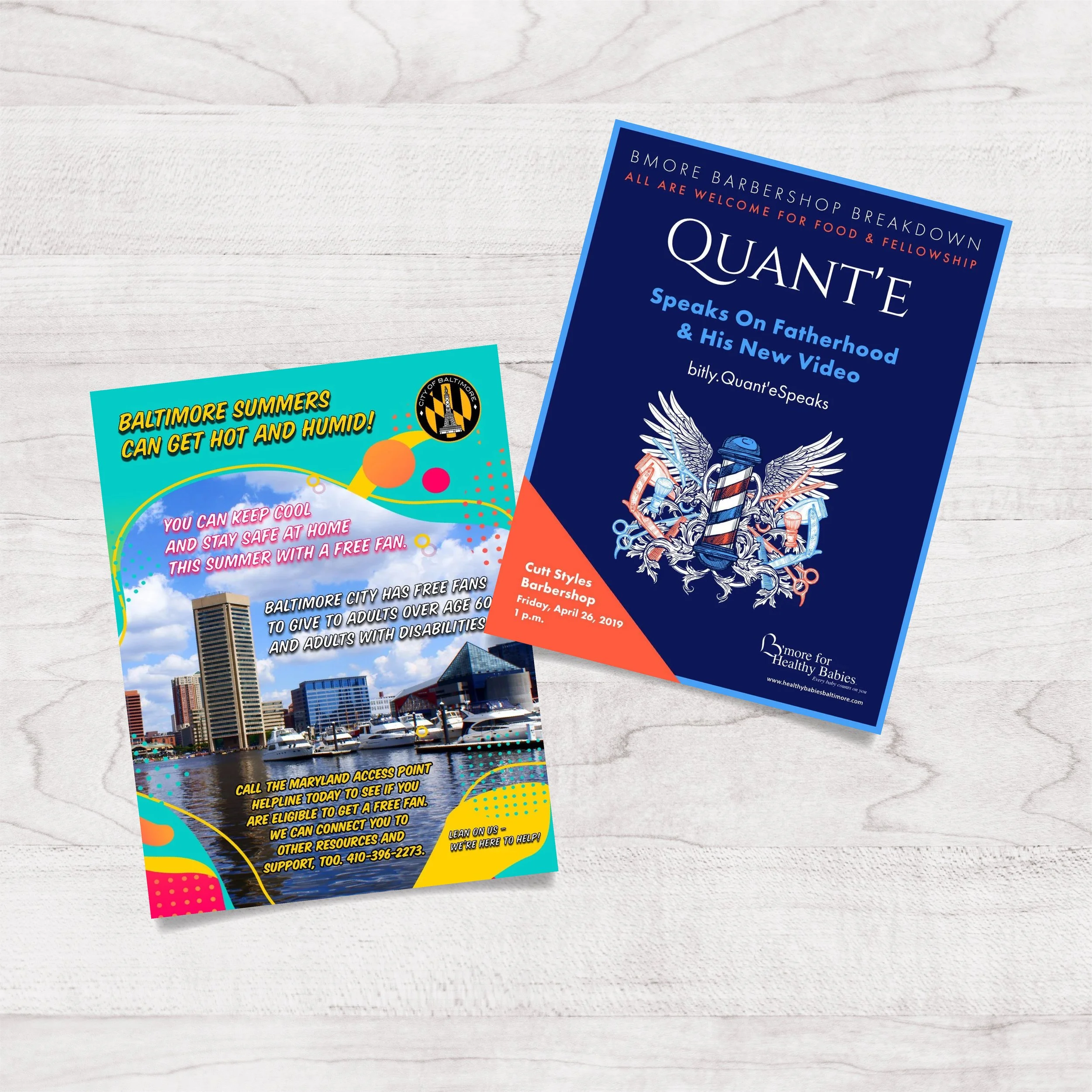 Flyers on a white wooden surface. The left flyer promotes Baltimore summers, staying cool, and free fans for adults over 60 and those with disabilities; includes an image of Baltimore's skyline and harbor. The right flyer advertises a barber shop eve