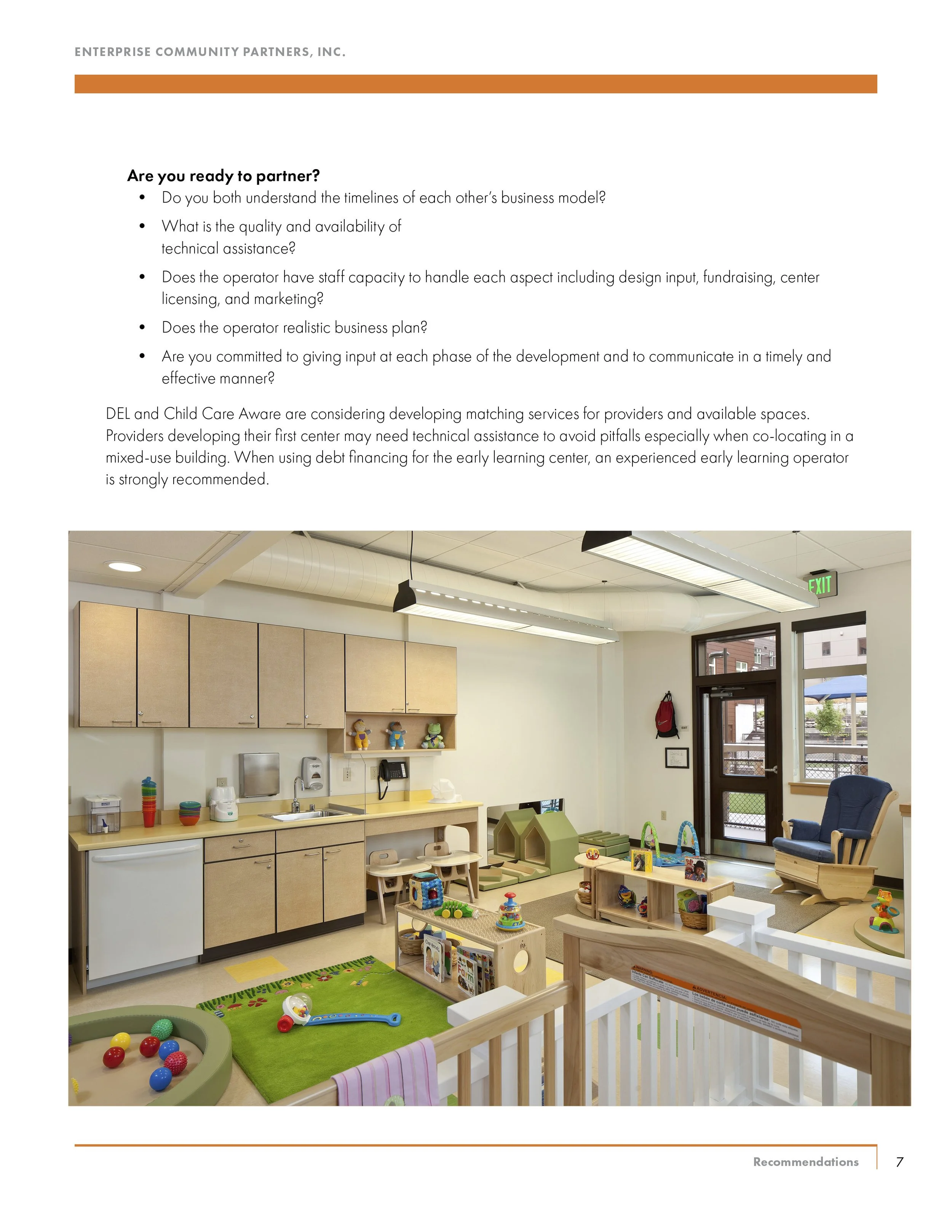 Children's play area with toys, books, and play structures in a room with cabinets, a rocking chair, and a door leading outside.