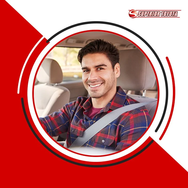 A smiling man sitting in the driver's seat of a car with a seatbelt on, inside a vehicle with a background of a sunny outdoor scene, and a graphic design featuring red, white, and black elements with the text "Superior Toyota."