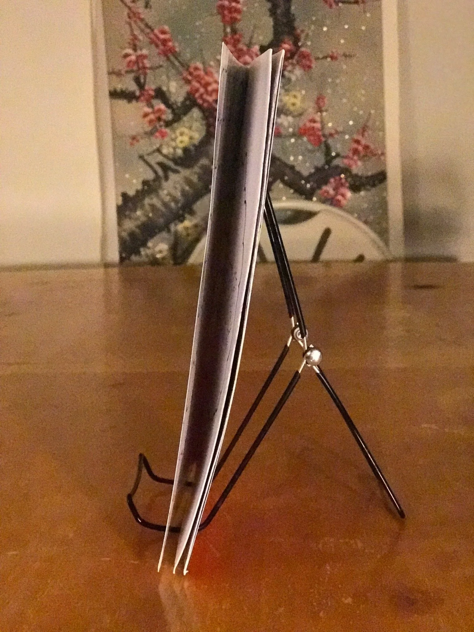 Books on a black metal stand on a wooden table with a decorative Asian-style clock and pink cherry blossom artwork in the background.