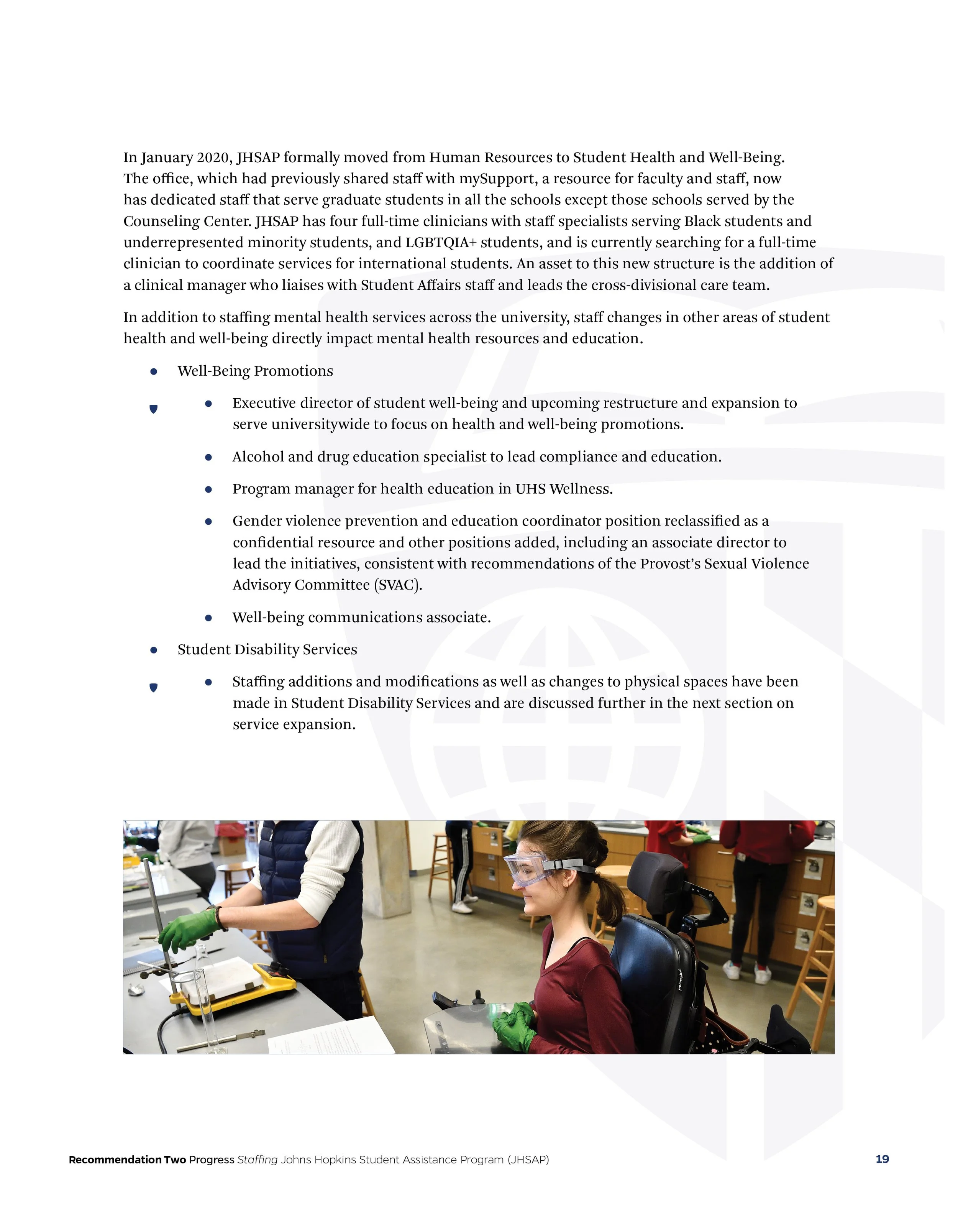A college student in a wheelchair wearing safety goggles and green gloves, participating in a science experiment in a classroom.