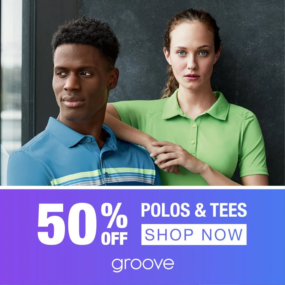 A man and woman wearing casual polo shirts standing indoors near a window. The woman has her arm around the man's shoulder. The image is an advertisement for a 50% off sale on polos and tees from groove.