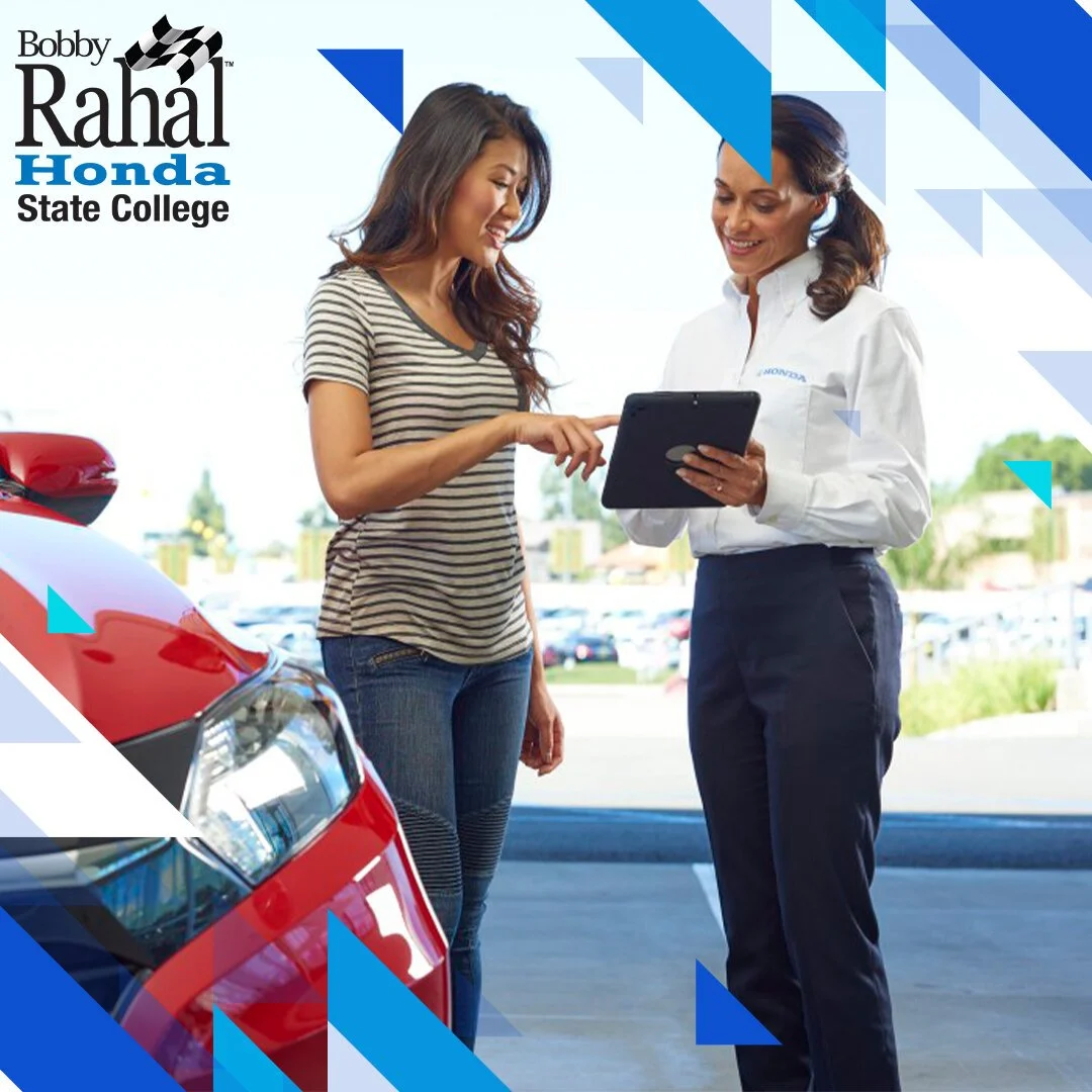 A woman and a car salesperson (or service advisor) are smiling and looking at a tablet inside a car dealership lot. There is a red car nearby, and the scene is bright with clear skies.