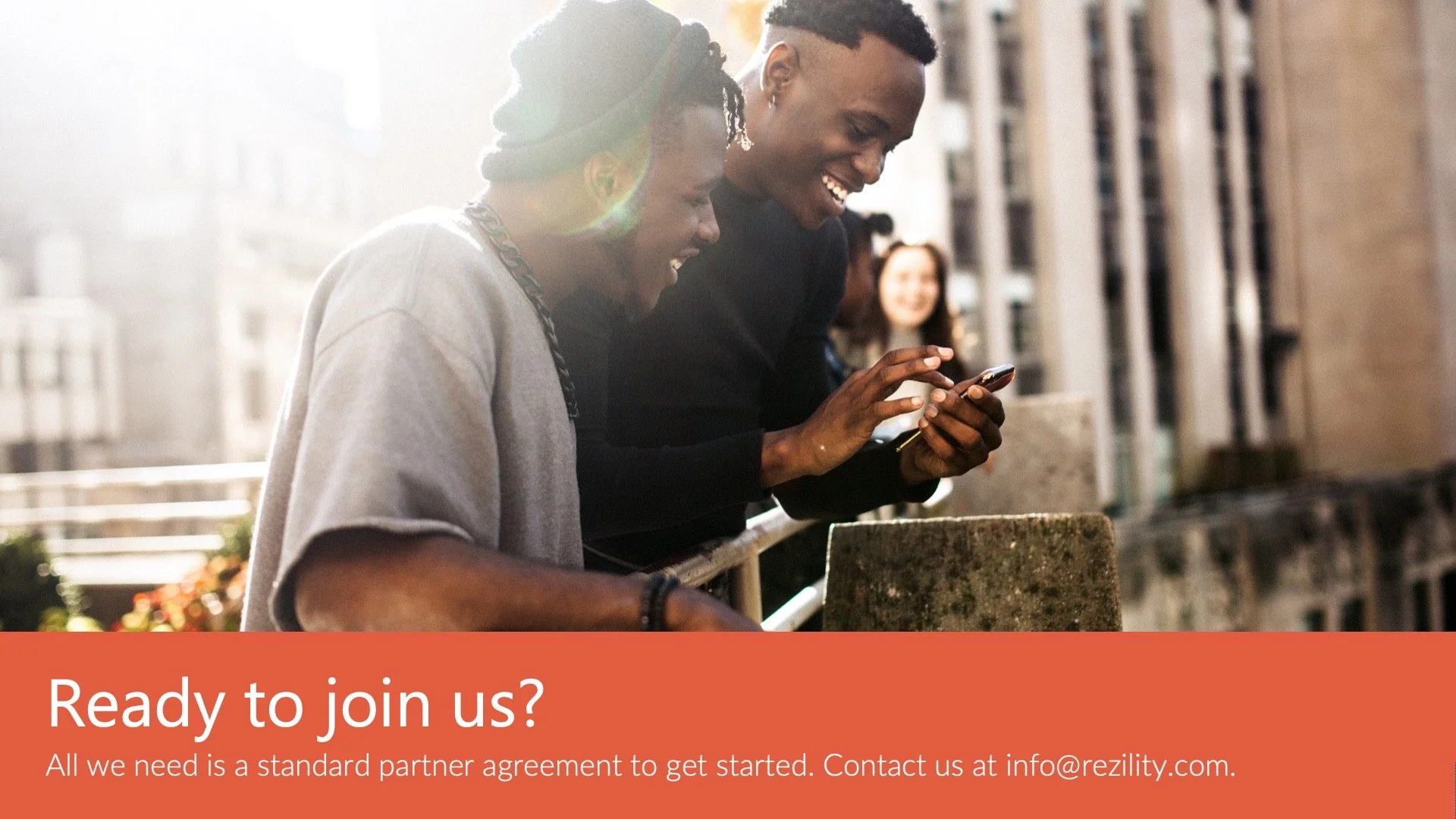 Two men laughing and using a smartphone outdoors, with a woman in the background, in front of a building, with a banner at the bottom that says 'Ready to join us?' and contact information.