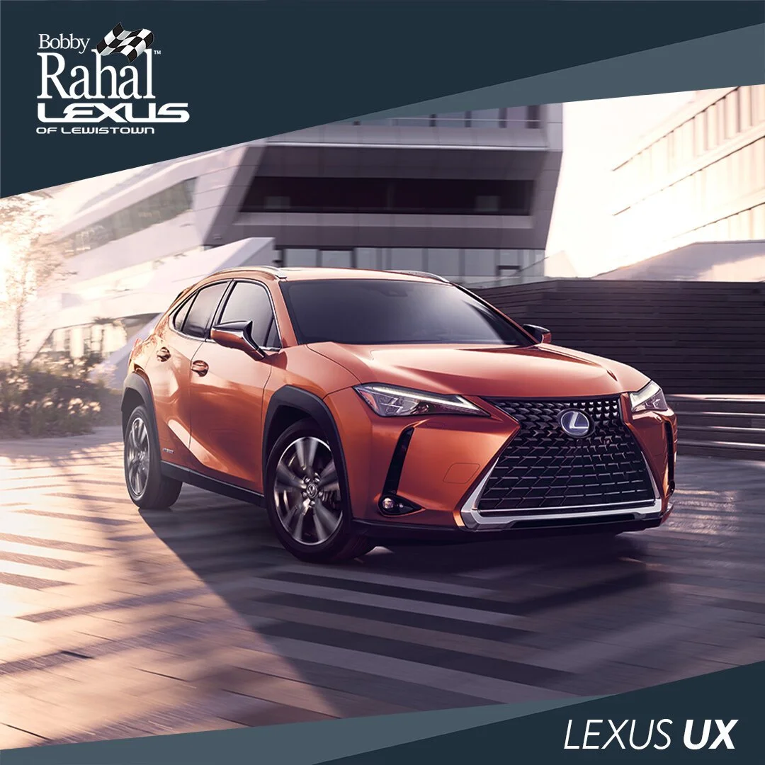 A copper-colored Lexus UX SUV driving on a city street with modern buildings in the background.