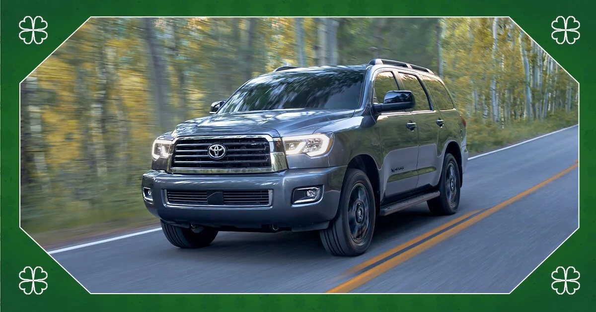 A gray Toyota SUV driving on a two-lane road through a forested area during daytime.