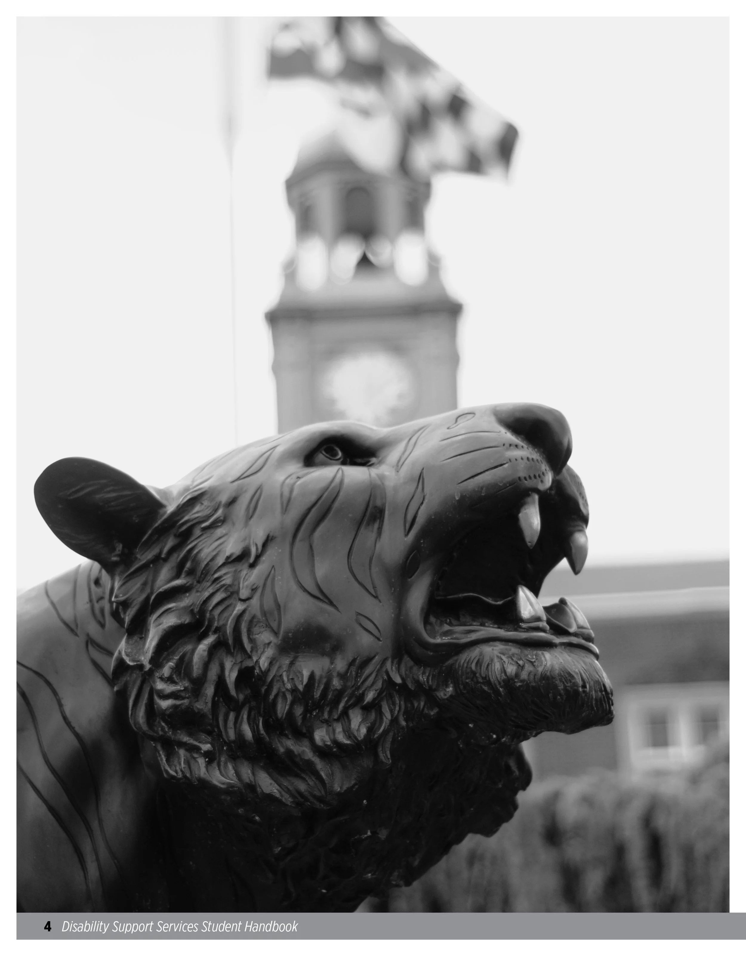 Black and white photo of a lion statue with its mouth open, showing teeth and detailed mane, with a clock tower in the blurred background.