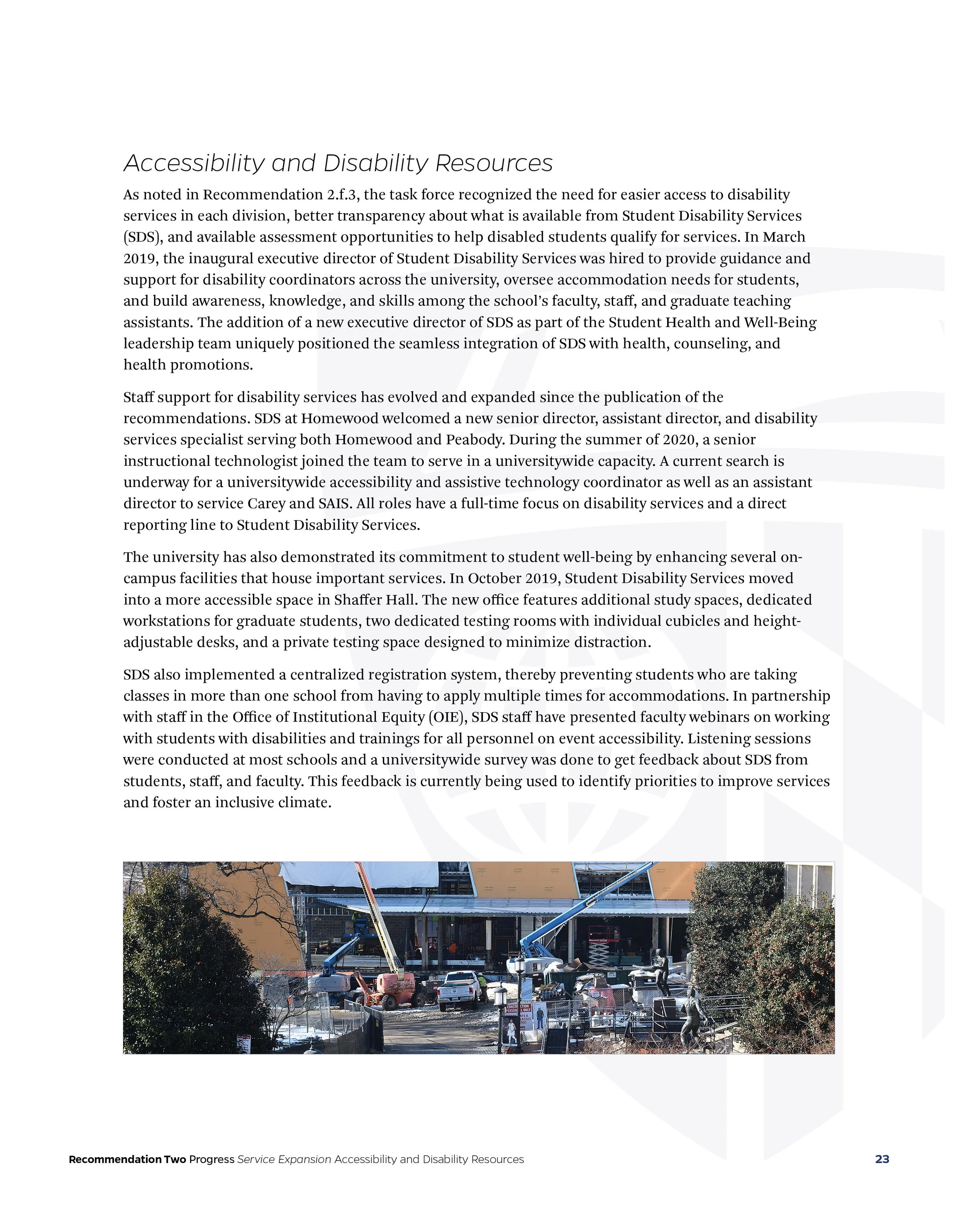 Photograph of a construction site with cranes, vehicles, and trees in front of a building.