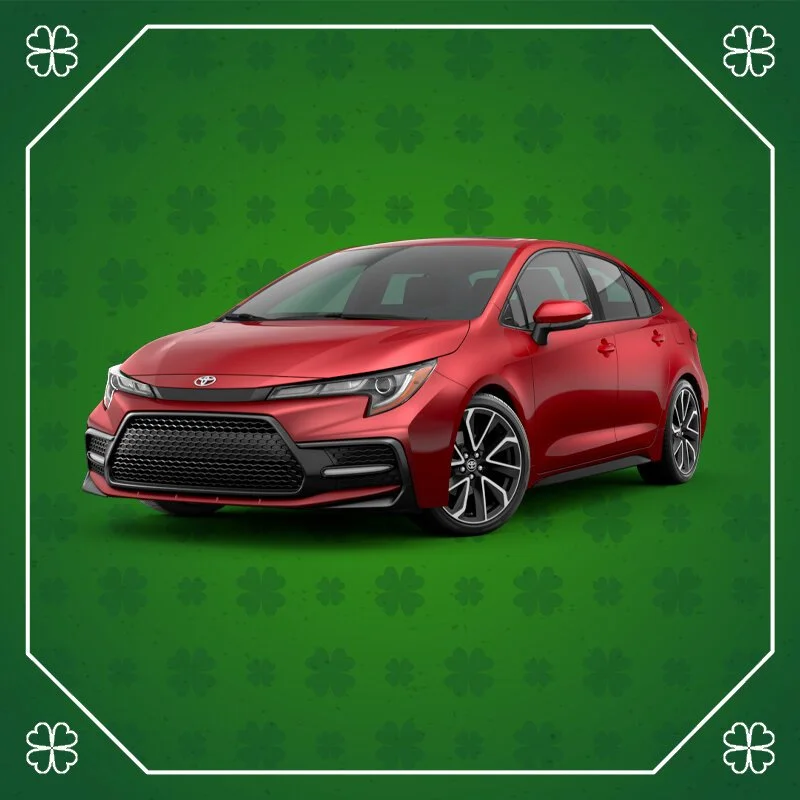 Red sedan car, likely a Toyota, on a green background with a festive, shamrock pattern and white border accents.