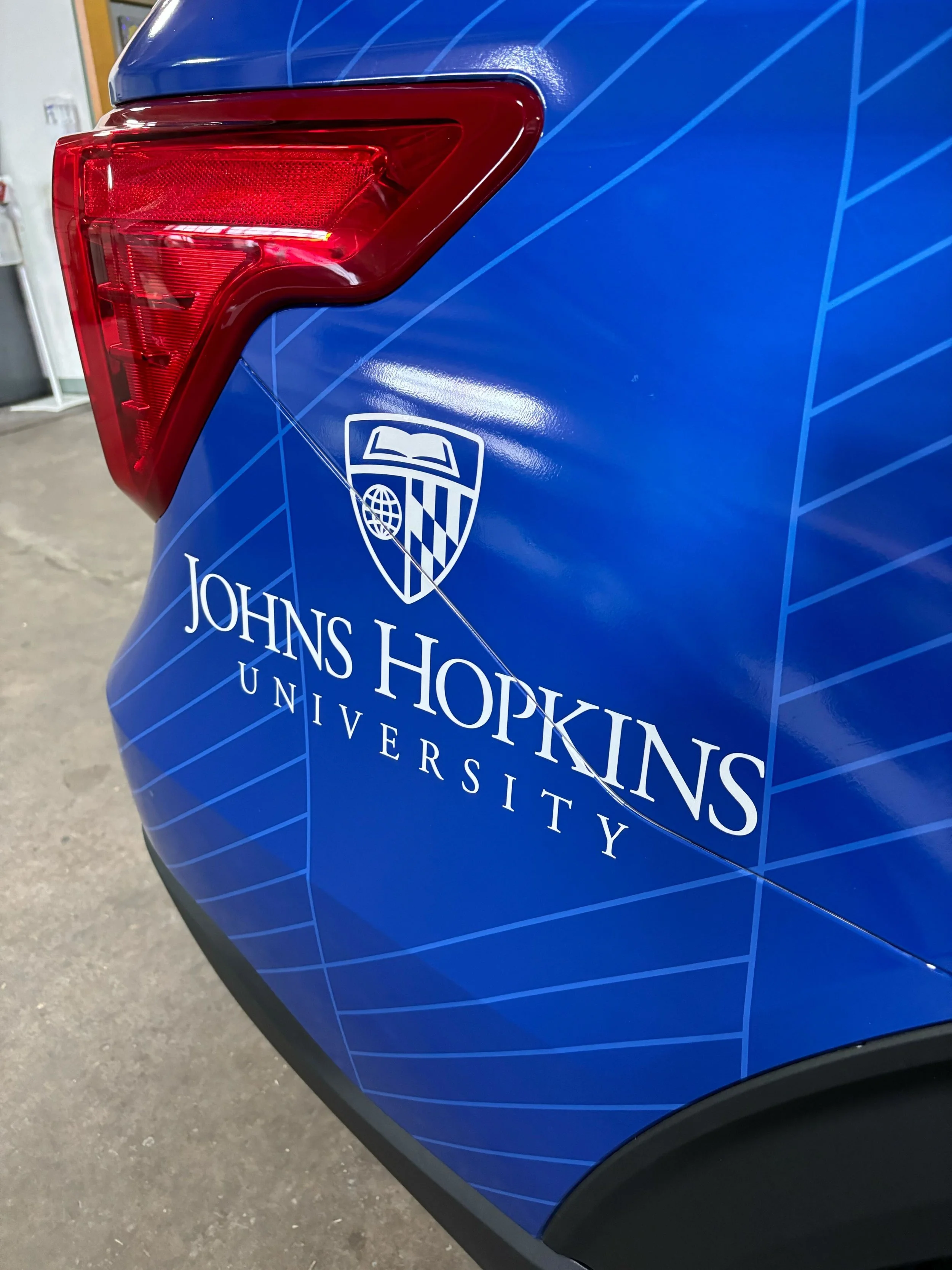 Close-up of a blue vehicle with Johns Hopkins University logo and text, showing a red taillight in the top left corner.